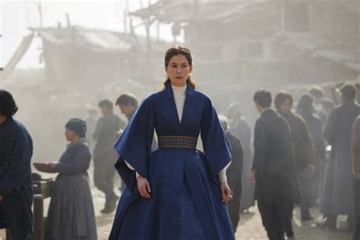 Moiraine stands in front of a crowd of commoners in a blue robelike dress in The Wheel of Time season 2.