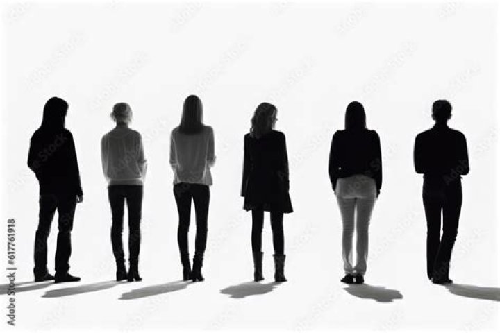 Several people seen from behind watch on a series of monitors as Katniss Everdeen gives the Mockingjay hand sign in The Hunger Games